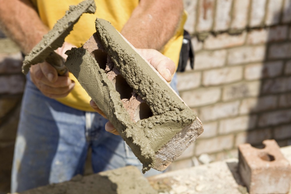 At left, a mason ‘butters’ a brick with mortar for installation in a masonry cavity wall. In the photo on the right, one can see the detail of a masonry cavity wall comprising a concrete-unit structural wall and brick veneer.