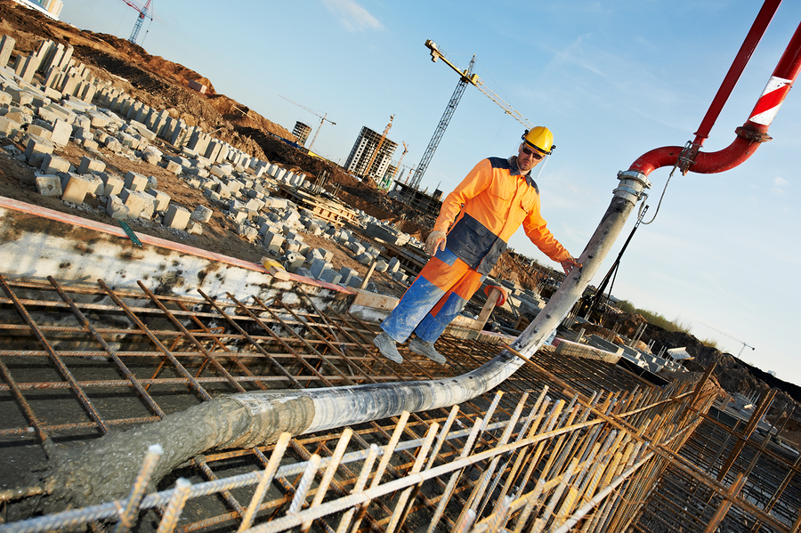 builder worker standing near trailer-mounted boom concrete pump on metal rods reinforcement of concrete casting formwork