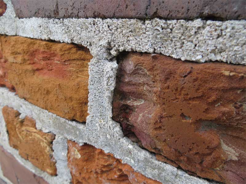 The exterior brick masonry exhibits surface erosion of the red/orange brick, revealing the unusual internal structure. The mortar is relatively hard and projects above the eroded surface of the adjacent brick units. Photos © David Patterson and Hugh Hou of WJE