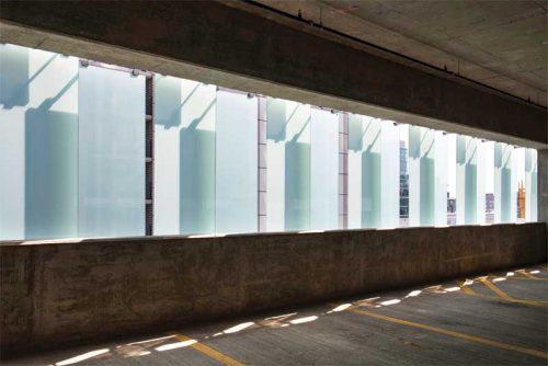 The translucent white laminated glass filters gentle, diffused daylight into the parking structure.