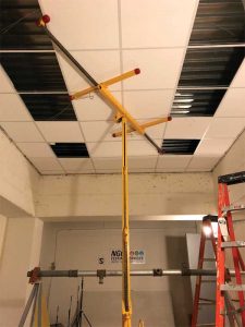 Figure 1: Following the baseline test of just the concrete floor slab (metal deck flutes visible through open parts of ceiling) a standard, metal, tee-bar, suspension grid, and ceiling panels were installed (in process).