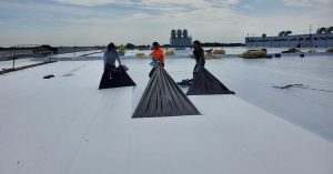 Three laborer applying Carlisle's APEEL Cover Tape to a roof.