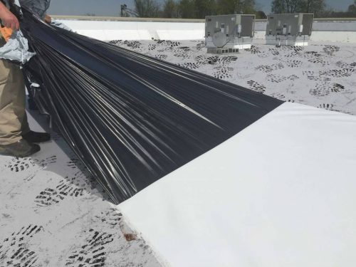 A man sticking Carlisle's APEEL Protective Film to a roof.