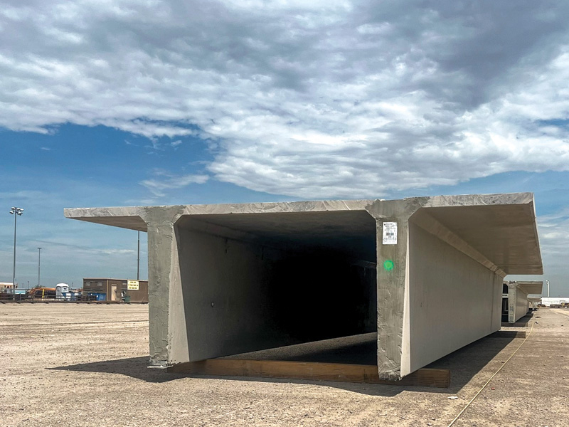 A large, gray concrete structure with a flat roof, set against a cloudy sky, sits on a barren lot, showcasing its hollow interior.