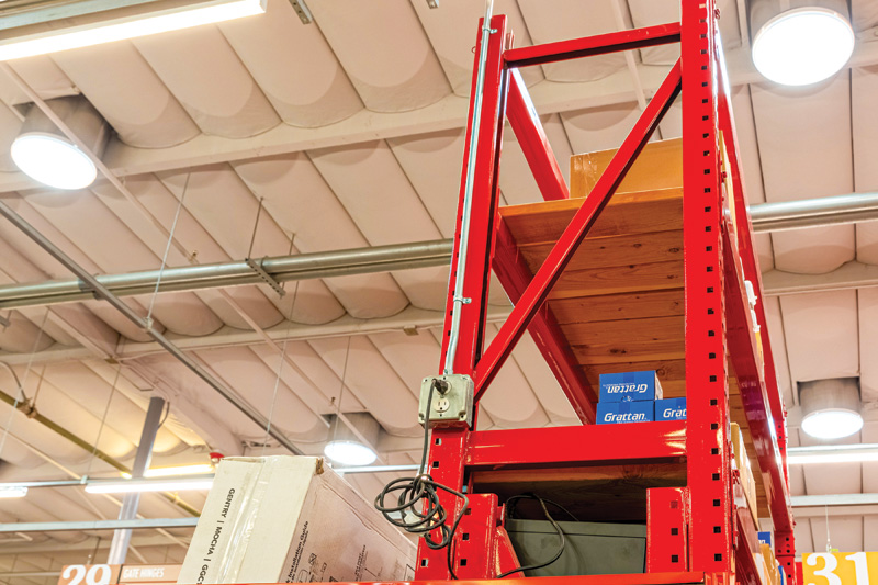 A tall red storage rack topped with wooden shelves, stocked with boxes, set in a well-lit retail space.