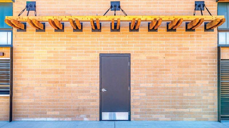 Brown door on a beige brick wall, topped with a wooden awning supported by black metal brackets.