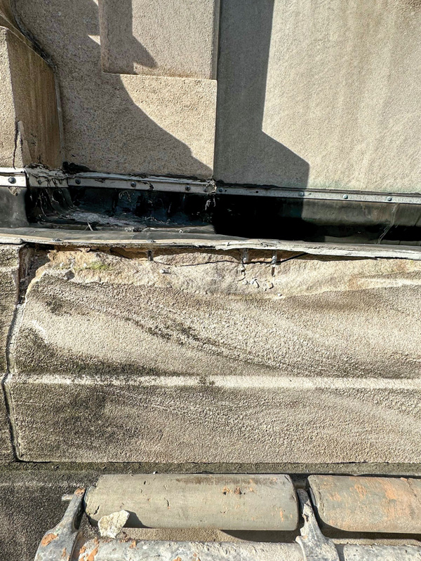 Close-up of worn stone wall with visible cracks and a metal flashing at the base, highlighting signs of weathering and repair needs.