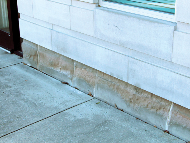 Close-up of a building's stone foundation, featuring smooth light-colored stone above and textured, weathered stone below.