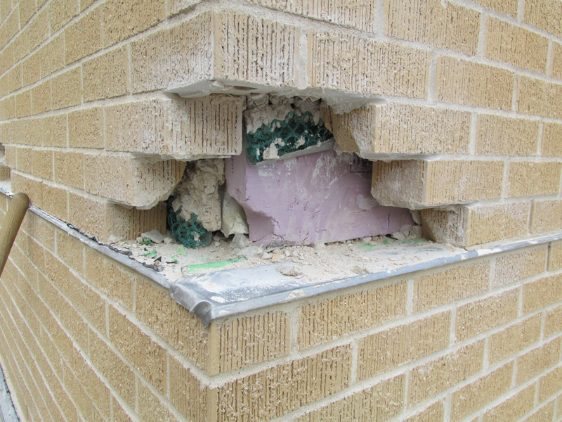 Damaged brick veneer wall exposing insulation and structural materials underneath.