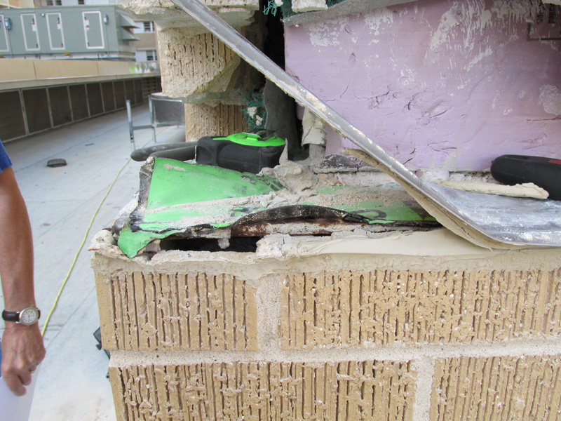 Close-up of damaged brick veneer wall showing bent metal flashing, exposed insulation, and deteriorated materials underneath.