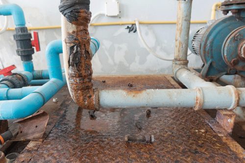 Corroded pipes and valves on a rust-stained metal surface, showcasing industrial wear and potential leaks in a mechanical area.