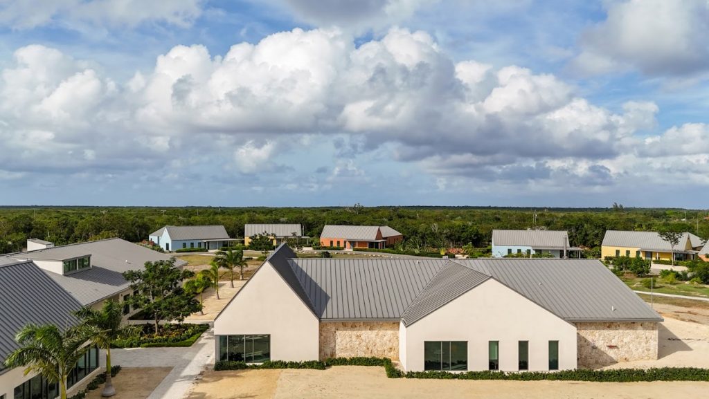 Aerial view of modern buildings with sloped roofs, surrounded by lush greenery and under a partly cloudy sky.