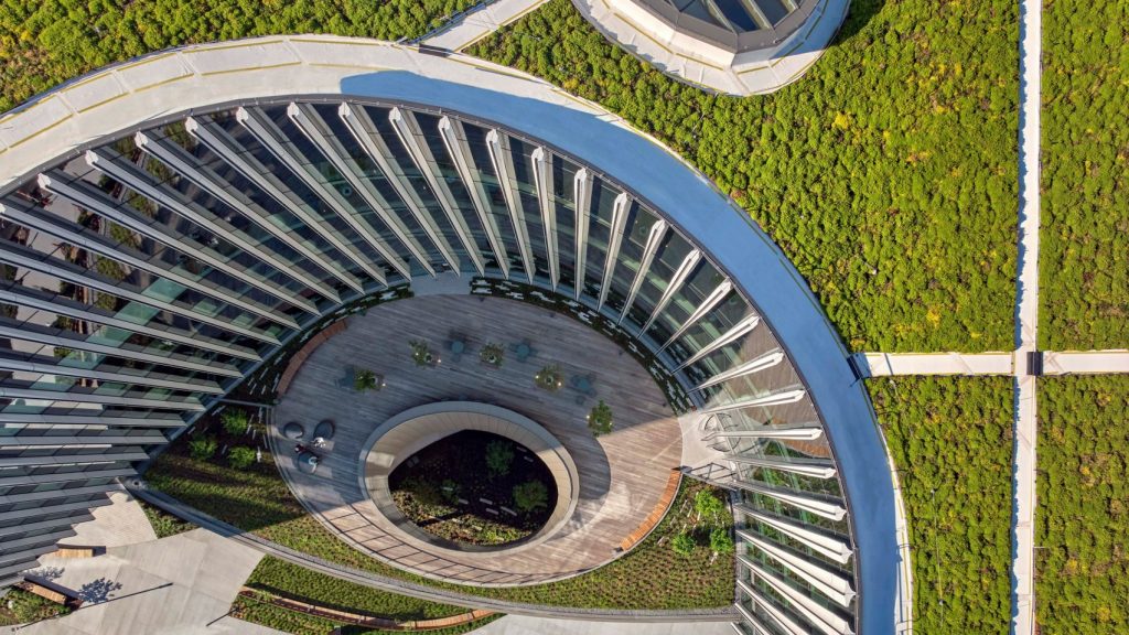 Aerial view of a modern circular courtyard surrounded by glass walls and a green roof with walking paths.