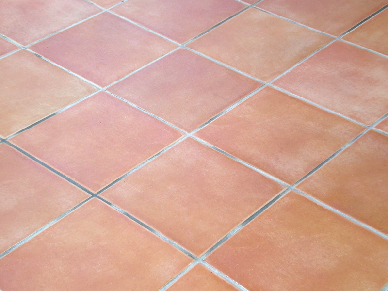 Close-up of a terracotta tile floor with a grid pattern, featuring warm orange hues and light grout lines between the tiles.