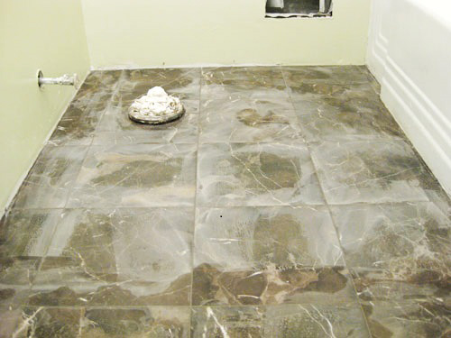 A newly tiled bathroom floor featuring dark, marbled tiles, with a drain and an unfinished wall area in the background.