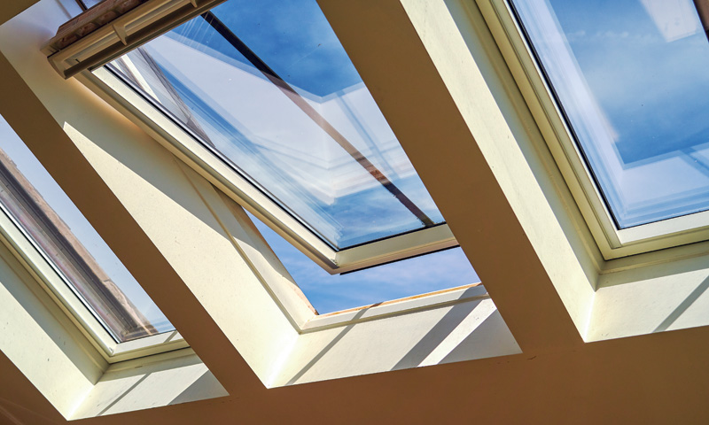 Four skylights set into a slanted roof, framing a bright blue sky and fluffy clouds, with daylight streaming into the room.