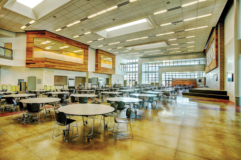 Spacious modern cafeteria with circular tables, vibrant natural light, and large windows showcasing a welcoming educational environment.