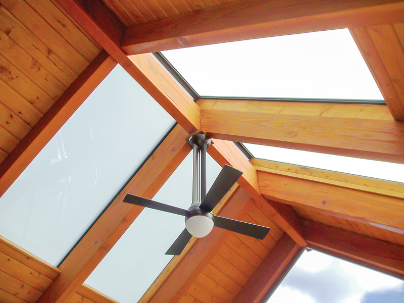 A ceiling fan hangs from a wooden beam structure beneath a skylight, providing light and ventilation.