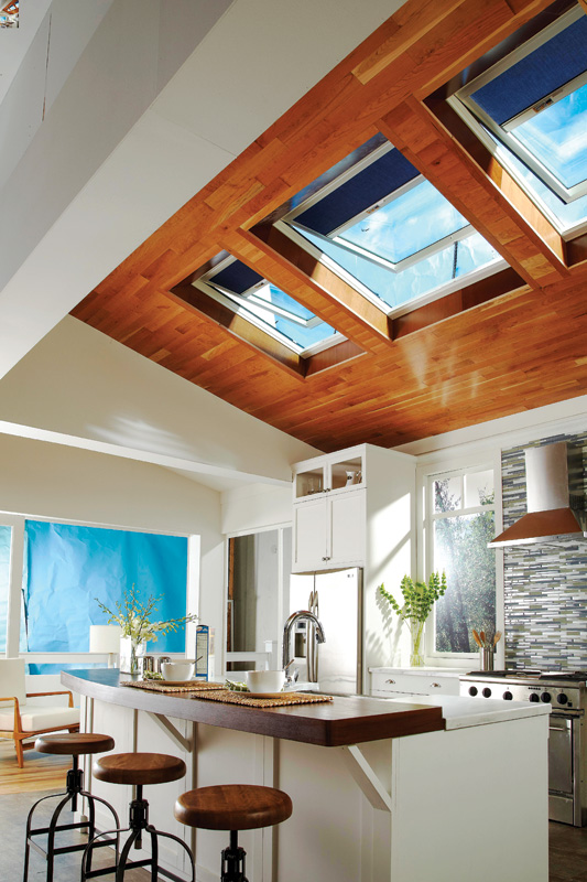 Bright, modern kitchen featuring a wooden ceiling with skylights, a sleek island, and stylish decor, bathed in natural light.