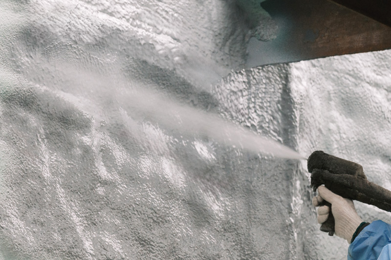 Close up of a contractor spraying waterproofing coating over closed-cell sprayfoam.