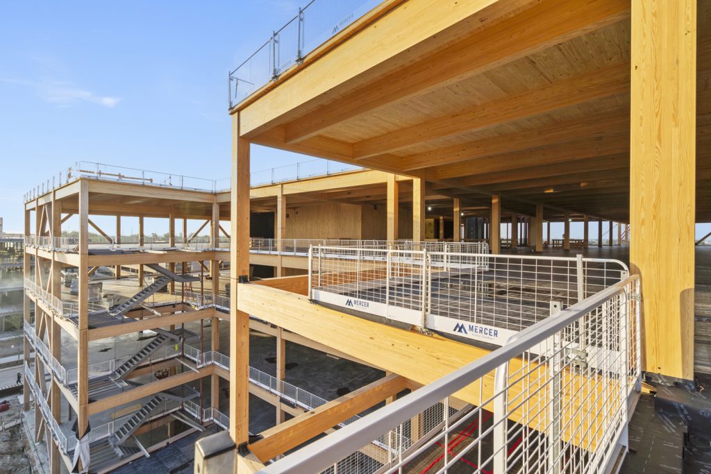 A partially constructed building showcasing wooden beams, spacious open levels, and safety railings against a clear blue sky.