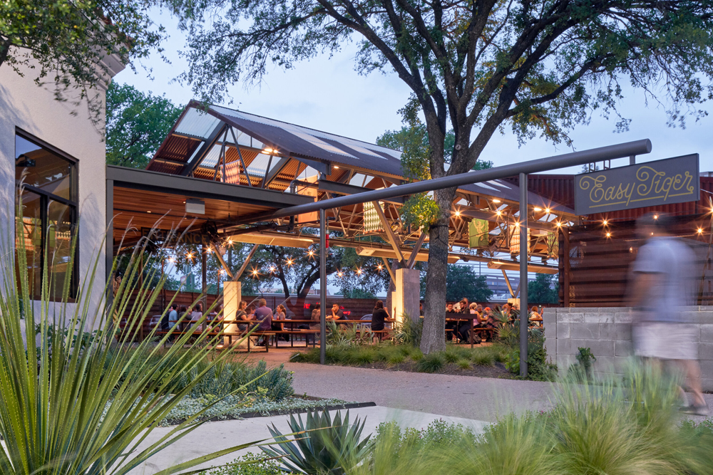 Outdoor dining area of Easy Tiger, with string lights and rustic architecture, filled with patrons enjoying the ambiance at dusk.