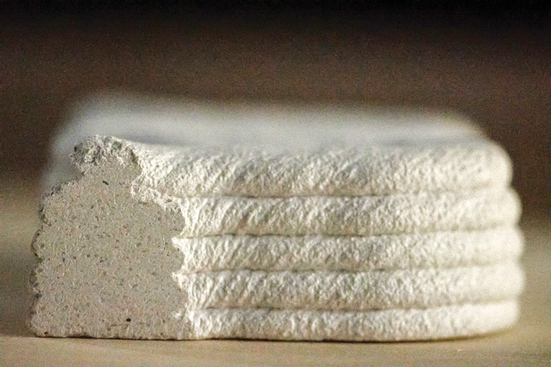 A stack of textured white paper or card, showing layered edges with a slight curve, on a softly lit surface.