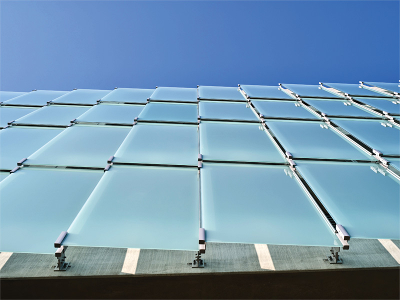 A close-up view of a modern building's glass facade, showcasing frosted panels against a clear blue sky.