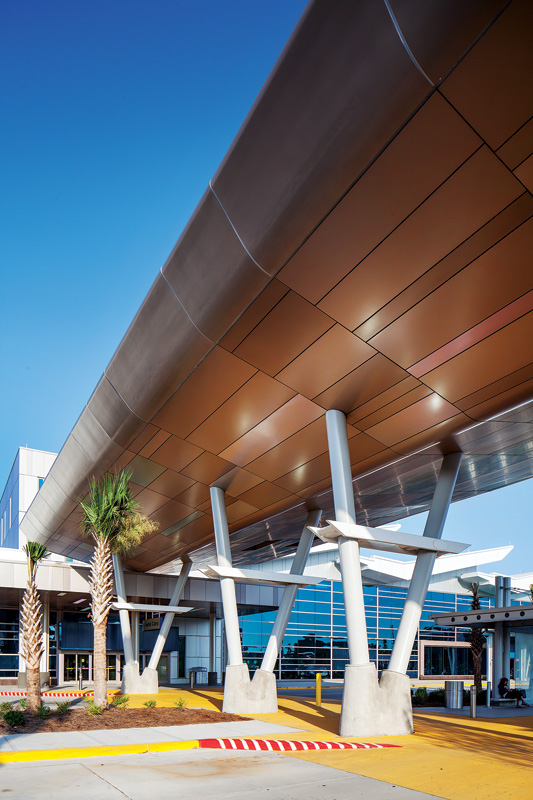Modern airport entrance featuring a sleek overhang, palm trees, and large glass windows under a clear blue sky.