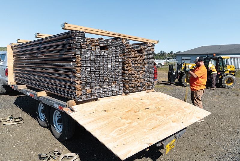 A worker in an orange shirt stands by a trailer loaded with stacked steel frames, preparing for transport in a construction area.
