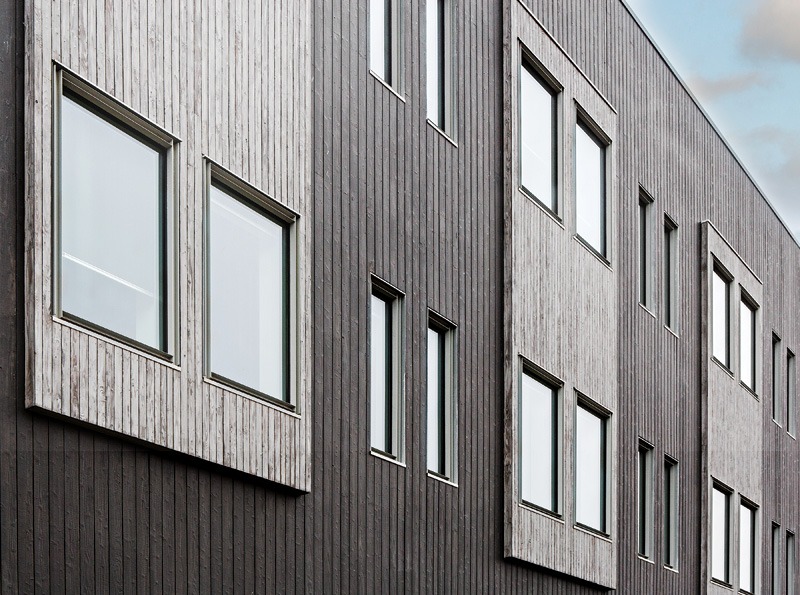 Close-up of a modern building facade featuring a mix of dark wood and lighter wooden paneling, with multiple large rectangular windows.