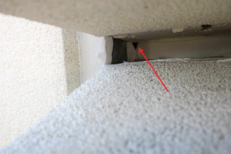 A close-up view of a gap between two surfaces, highlighted with a red arrow, revealing potential space for pest entry.