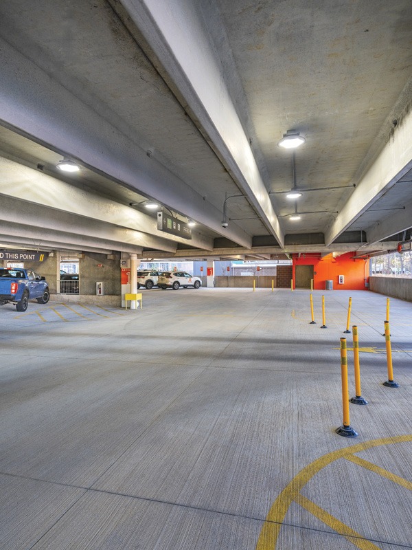 Empty parking garage with concrete beams, yellow poles, and illuminated signs. Modern design with minimal cars parked.
