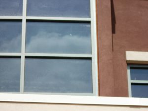 Close-up of a building's window reflecting white clouds, bordered by red-brown stucco. The image conveys a calm, urban atmosphere.
