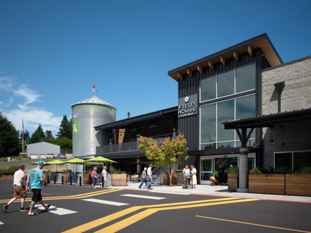 Modern building labeled "Field House" on a clear day, featuring large windows and a metallic silo. People walk by, creating a lively and welcoming atmosphere.