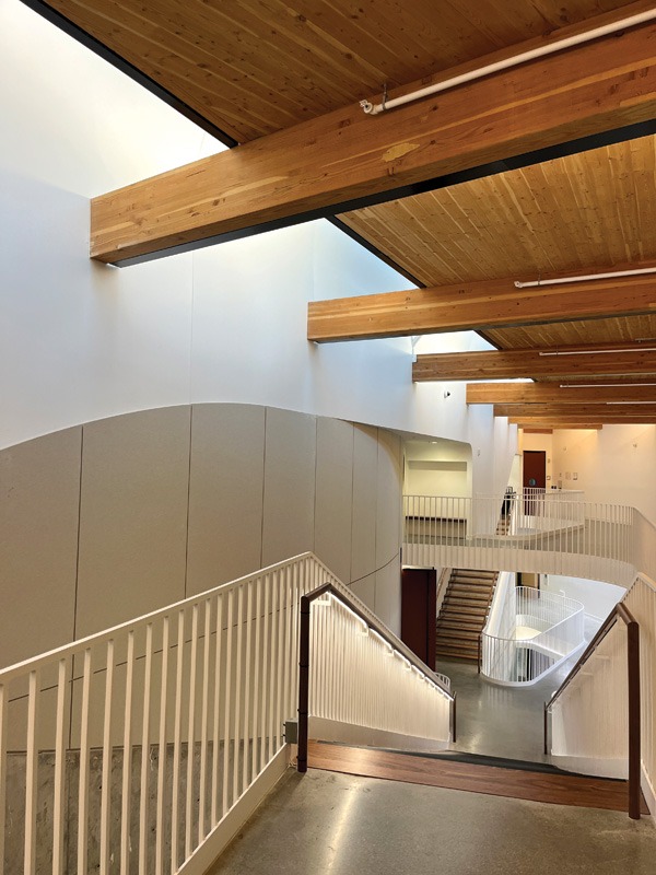 Modern indoor space featuring an elegant staircase with white railings, wooden ceiling beams, and curving walls, creating an open, airy atmosphere.