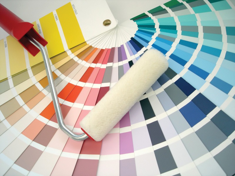A paint roller rests beside various paint samples arranged on a color wheel, showcasing a spectrum of colors.