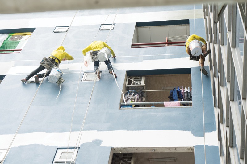 A group of workers cleaning windows on a high-rise building, using harnesses and equipment for safety.