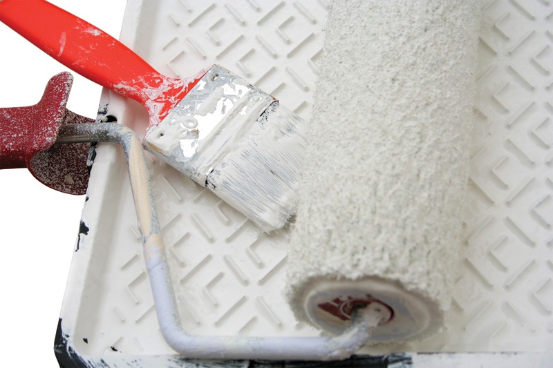 A paint roller and a brush resting on a white surface, ready for painting tasks.