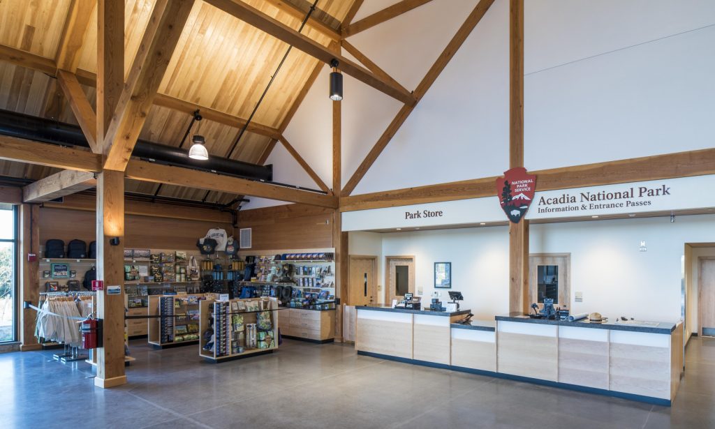 Spacious interior of Acadia National Park visitor center, featuring high wooden beams, a staffed information desk, and a well-stocked park store.