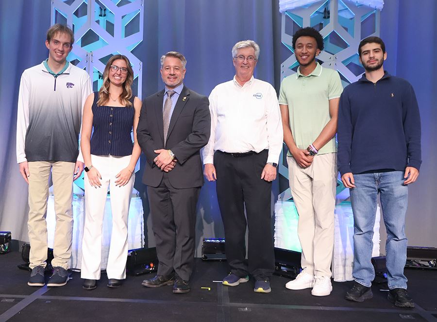 Six individuals stand on a stage, posed and smiling in front of geometric background structures.