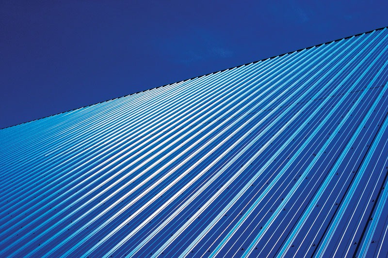 A low-angle view of a slanted corrugated metal surface reflecting blue hues against a clear sky.