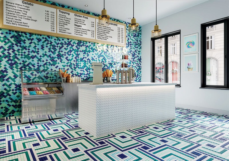 A colorful ice cream shop interior featuring a mosaic wall, a white serving counter with ice cream, and geometric patterned flooring.