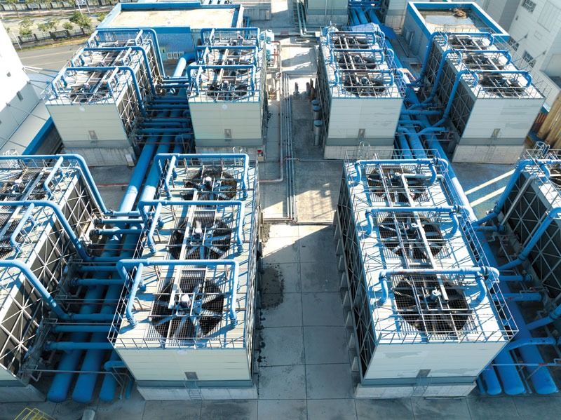 Bird's-eye view of an industrial cooling system featuring several large cooling units with black fan blades and blue piping.