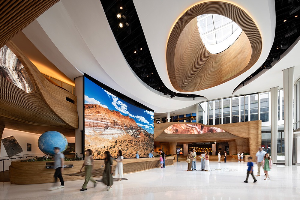 A modern building interior featuring a large digital landscape display, a round globe sculpture, and people moving through the open space.
