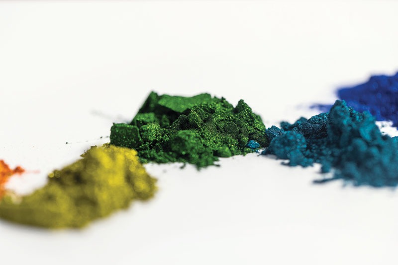 Colored powders in orange, yellow, green, teal, blue, and deep blue arranged in a line on a white surface.