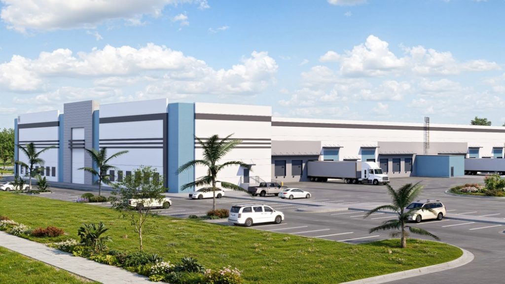 A modern industrial building with a light blue and white façade, surrounded by a green lawn and palm trees, featuring a parking lot with various vehicles including a delivery truck.