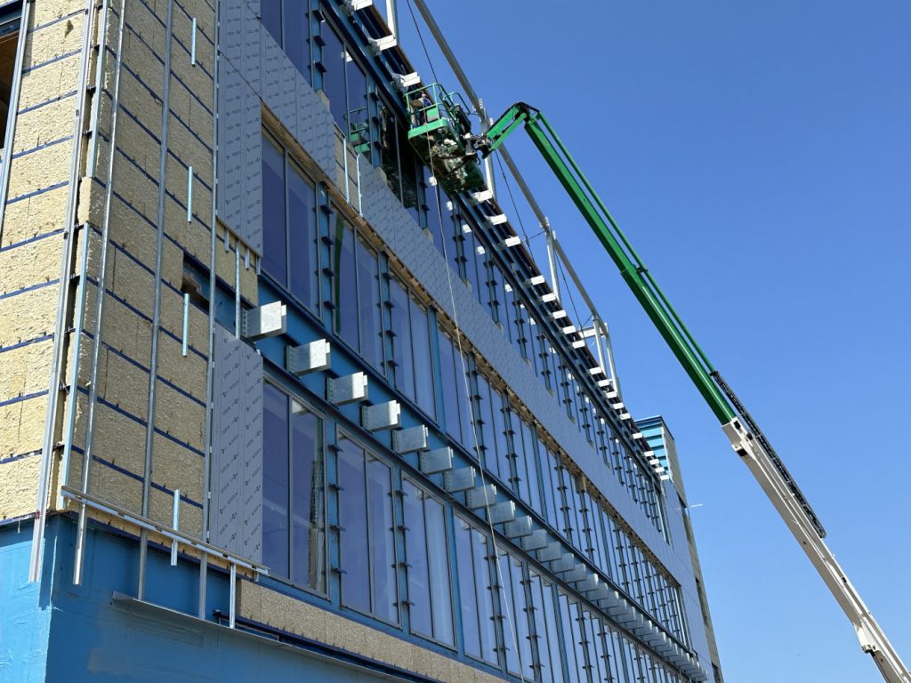 Construction workers’ lifts beside a partially clad multistory building under a clear blue sky.