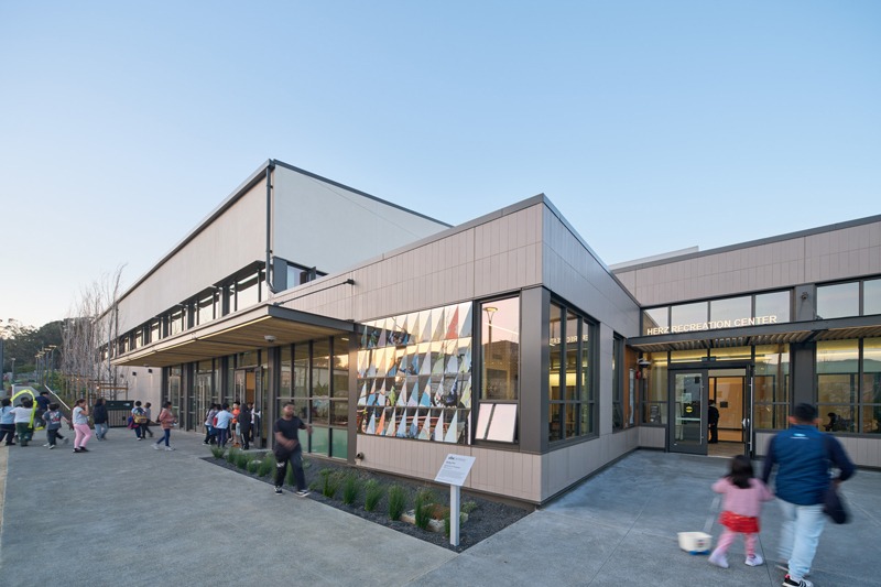 Modern Herz Recreation Center with colorful geometric window artwork and people gathered outside.