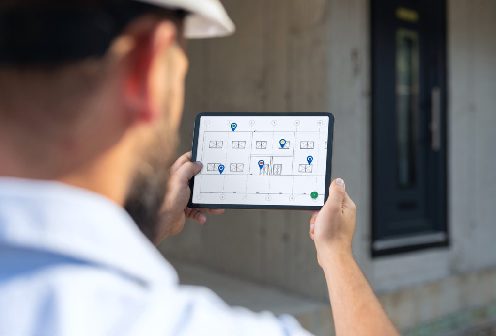 Person in a hard hat viewing a tablet displaying a building floor plan with multiple location pins.